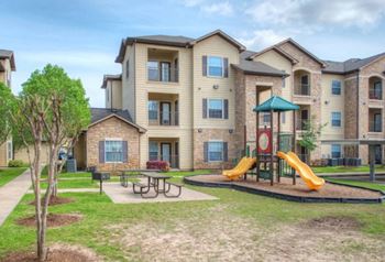 a playground with a swing set and picnic table in front of an apartment building